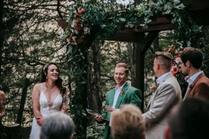 A couple exchanges vows during an outdoor garden wedding ceremony under a floral-decorated wooden arbor.