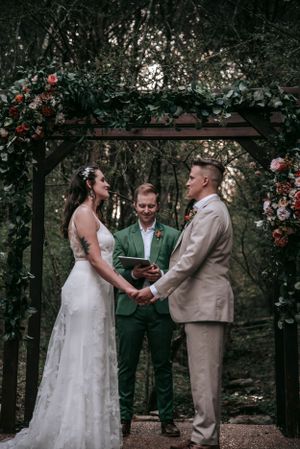Wedding ceremony under rustic wooden arbor with climbing roses in a forest setting.