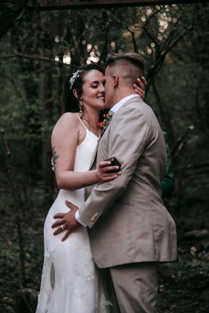 Newlyweds share intimate moment under garden arbor during outdoor wedding.
