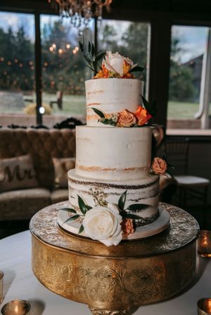 Elegant three-tier white wedding cake decorated with peach and white roses on a gold stand.