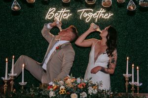 A wedding couple poses in front of a green wall with neon 'Better Together' sign.