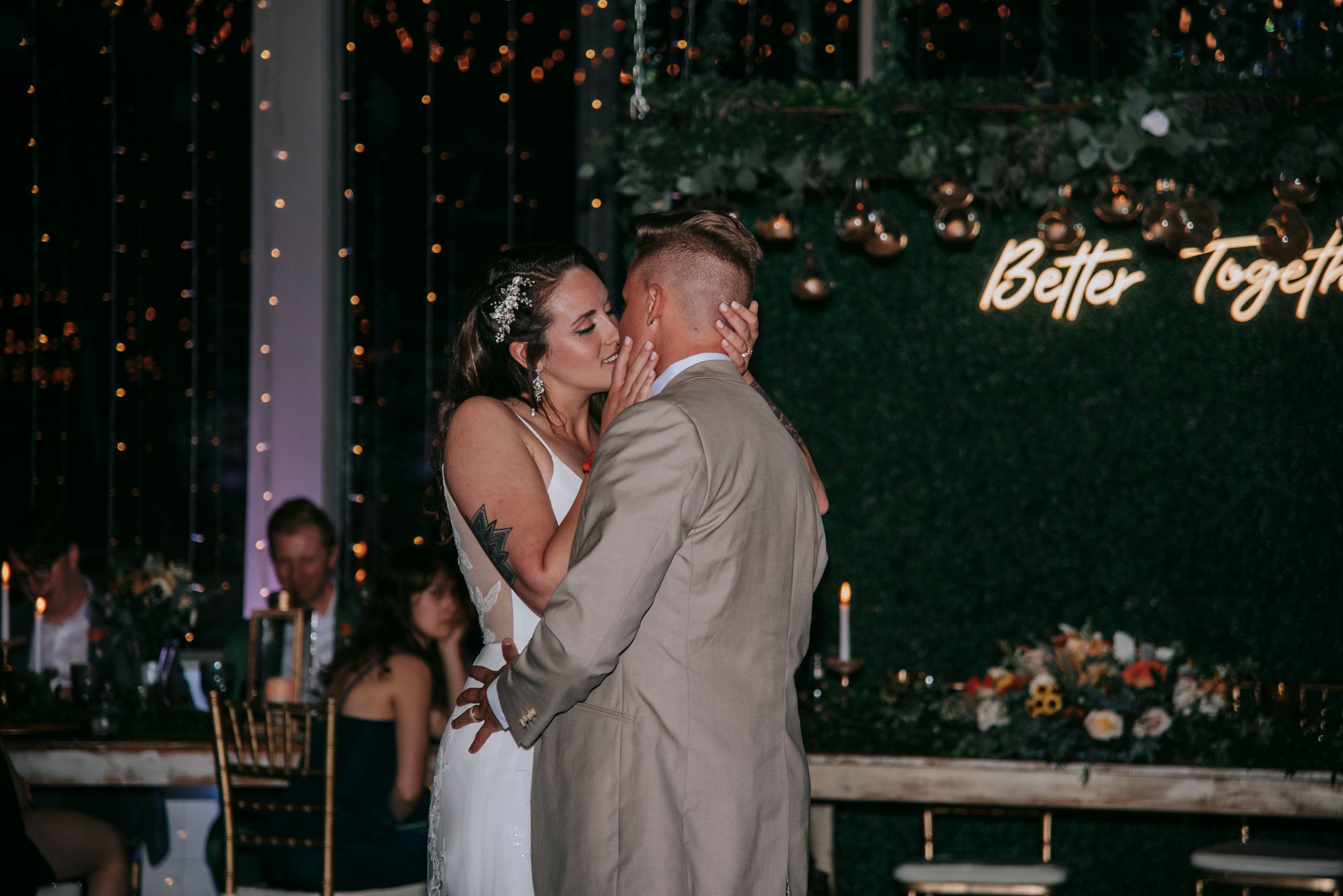 Romantic dance moment under a neon 'Better Together' sign at wedding reception.
