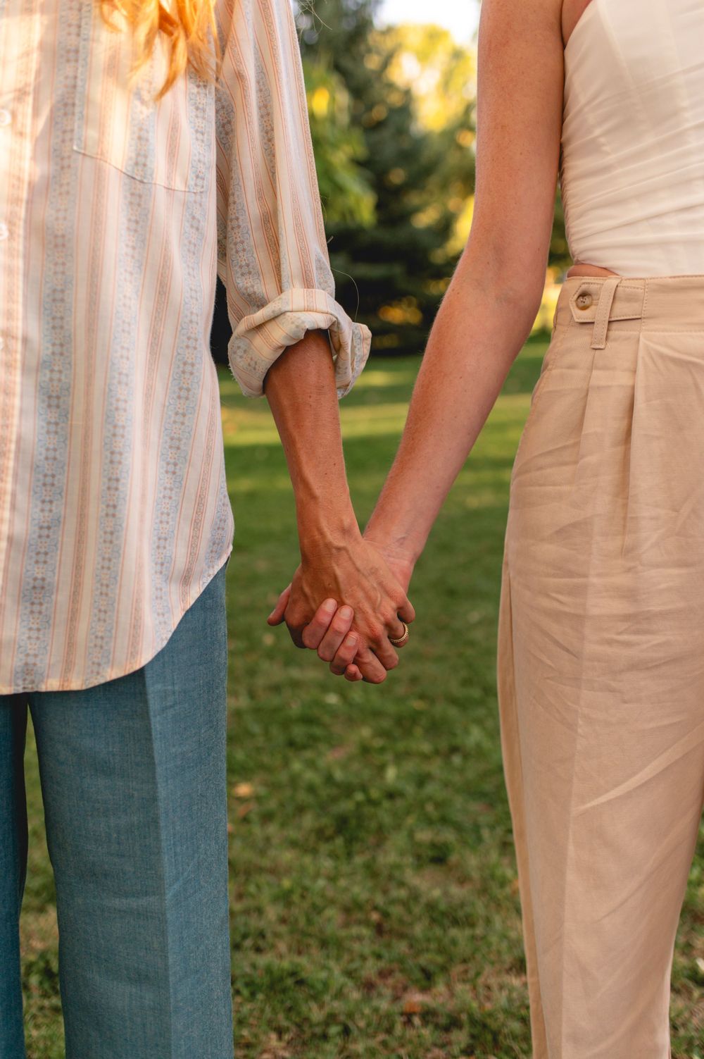 Close-up view of two people holding hands outdoors in casual attire against a sunlit garden background.