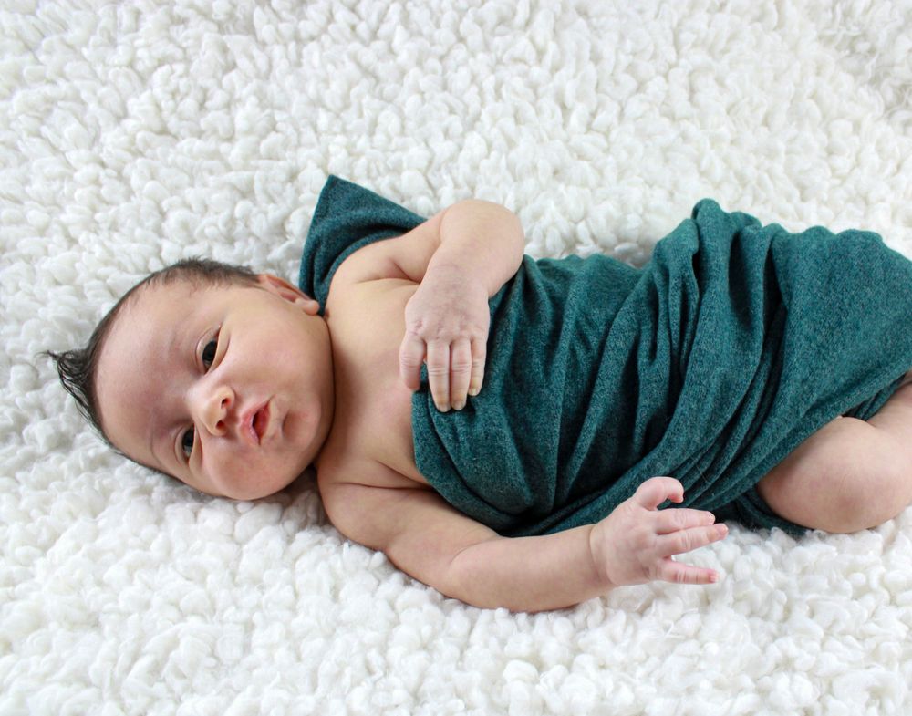 Baby wrapped in teal cloth laying on white furry blanket.