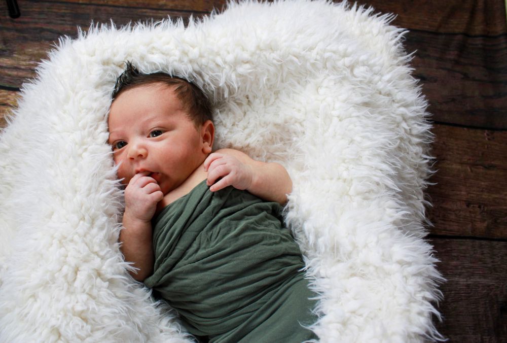 Baby in sage green wrap nestled on white fur rug.