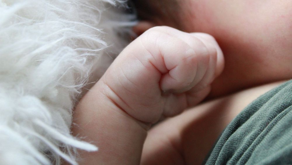 Close-up of tiny baby hand against white furry fabric.
