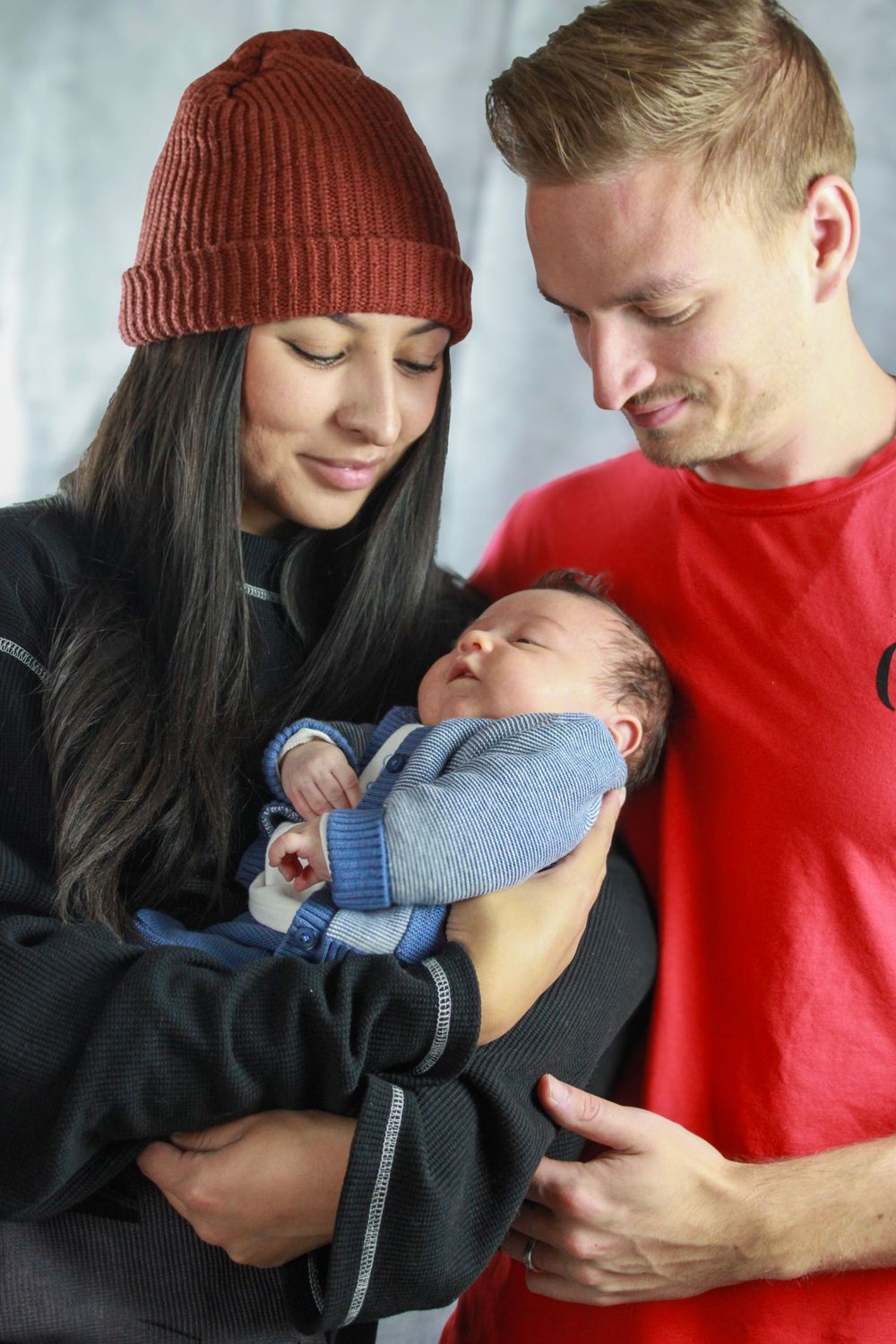 Family poses together as parents admire their sleeping baby in blue cardigan.