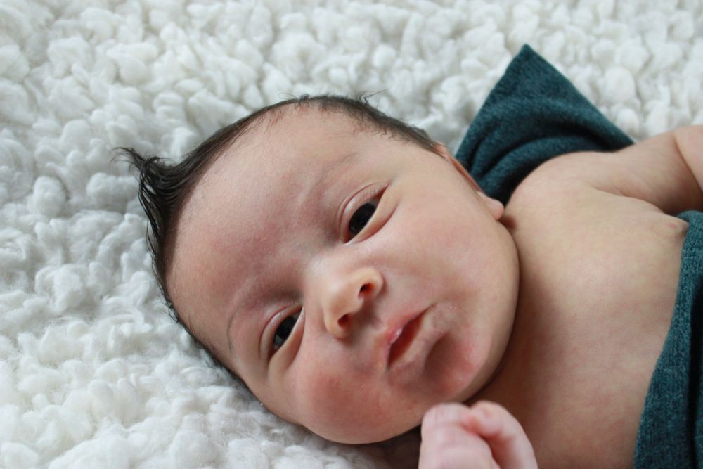 A newborn infant lying on a soft white blanket wearing a teal wrap.