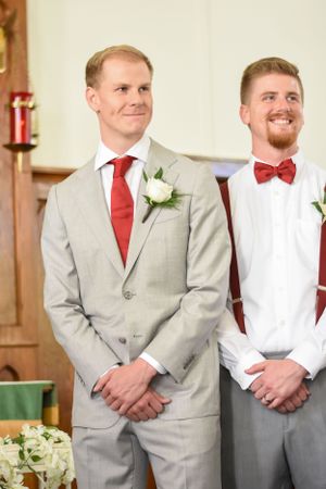 A groom and his best man smiling as he looks toward his bride walking down the aisle
