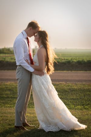 a couple who has just gotten married standing in front of the sunset with their foreheads touching.