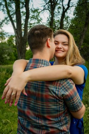 A couple hugging. The woman is looking at the camera smiling while her arms are around her partner's neck.