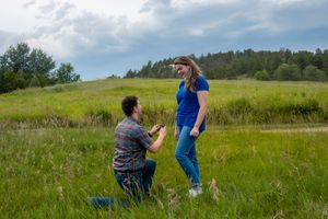 A man on one knee proposing to a woman in a blue shirt and jeans.