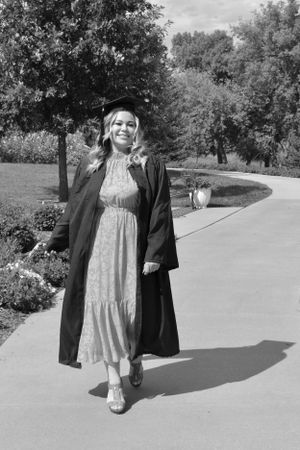 A woman wearing a cap and gown walking down a sidewalk. the photo is black and white.