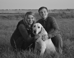 A mom, son and their yellow lab in a grassy field. The photo is black and white.