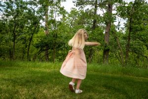 A young girl in a pink dress spinning outside. Her face is not visible.