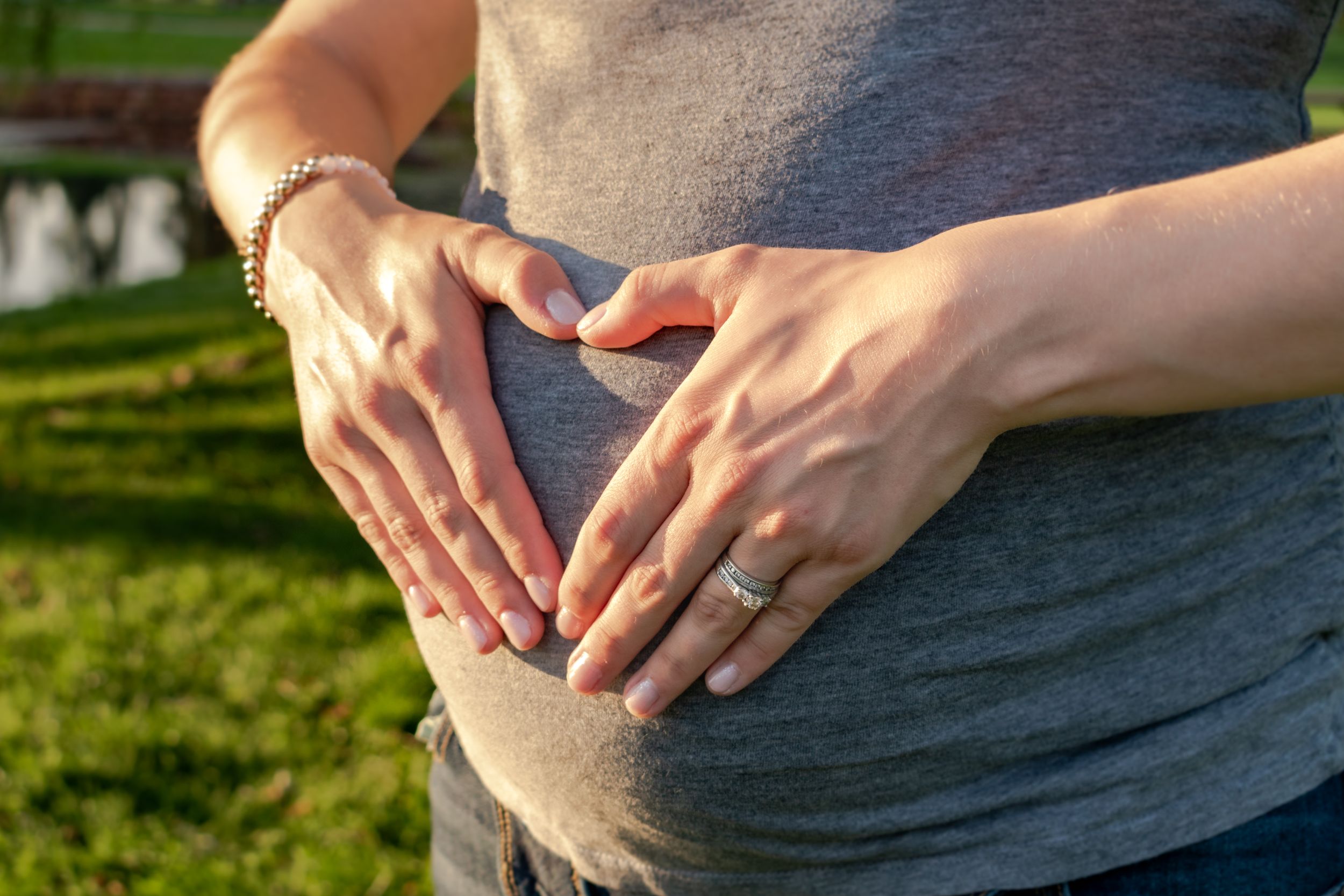 A woman making the shape of a heart on her pregnant belly.
