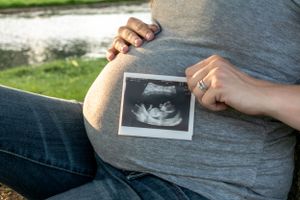 A pregnant woman holding her ultrasound photo in front of her belly.