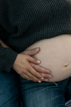 A closeup of a pregnant belly with the mom and dad's hands resting on the side.