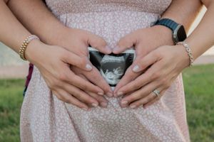 A couple holding an ultrasound picture in front of the mom's pregnant belly.