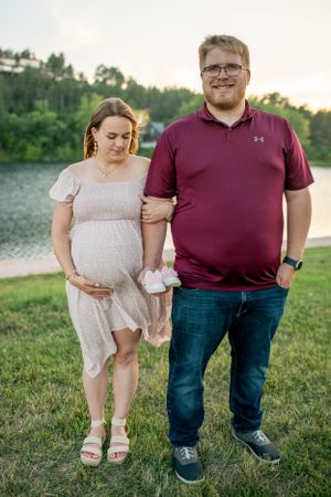 A couple standing side by side in front of a lake, the woman is pregnant.