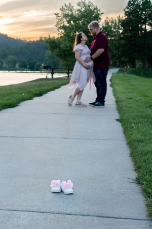 A couple standing in the background with a pair of pink baby shoes on the sidewalk in the foreground.