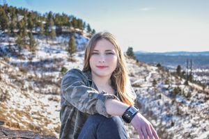 A young woman posing on a mountain side with her arm draped across her knee