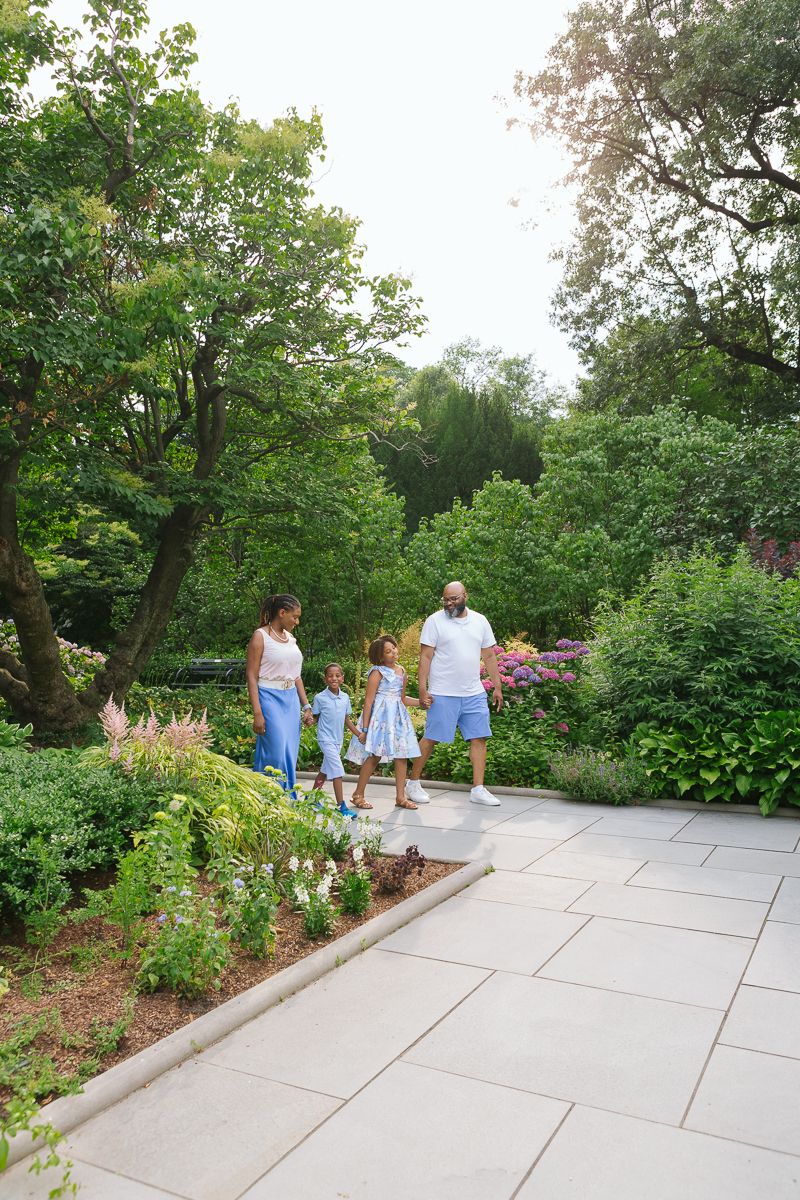 Family of four strolling through Central Park garden candidly in summer light