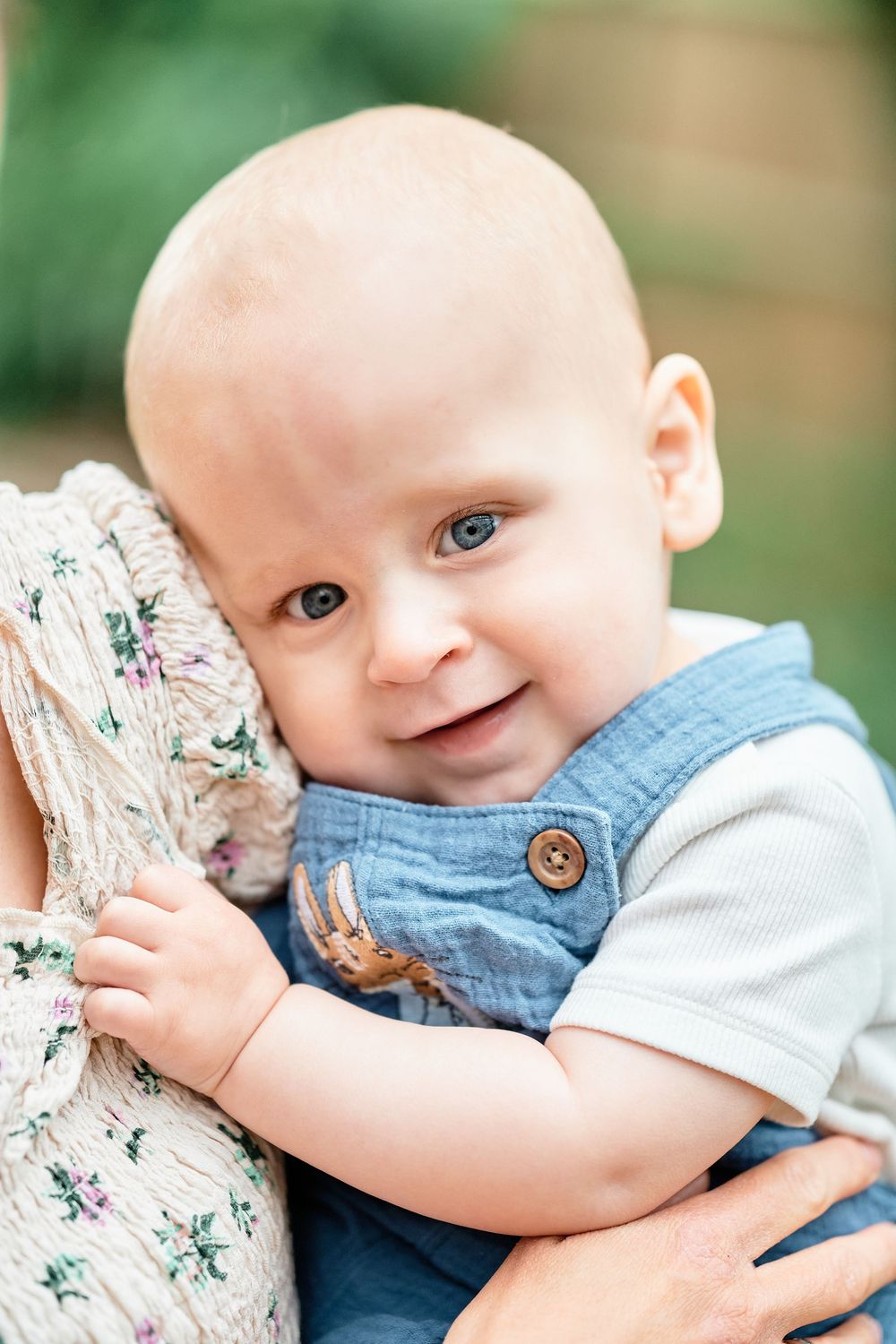 Small child in blue denim outfit hugs floral print cushion while smiling at the camera.