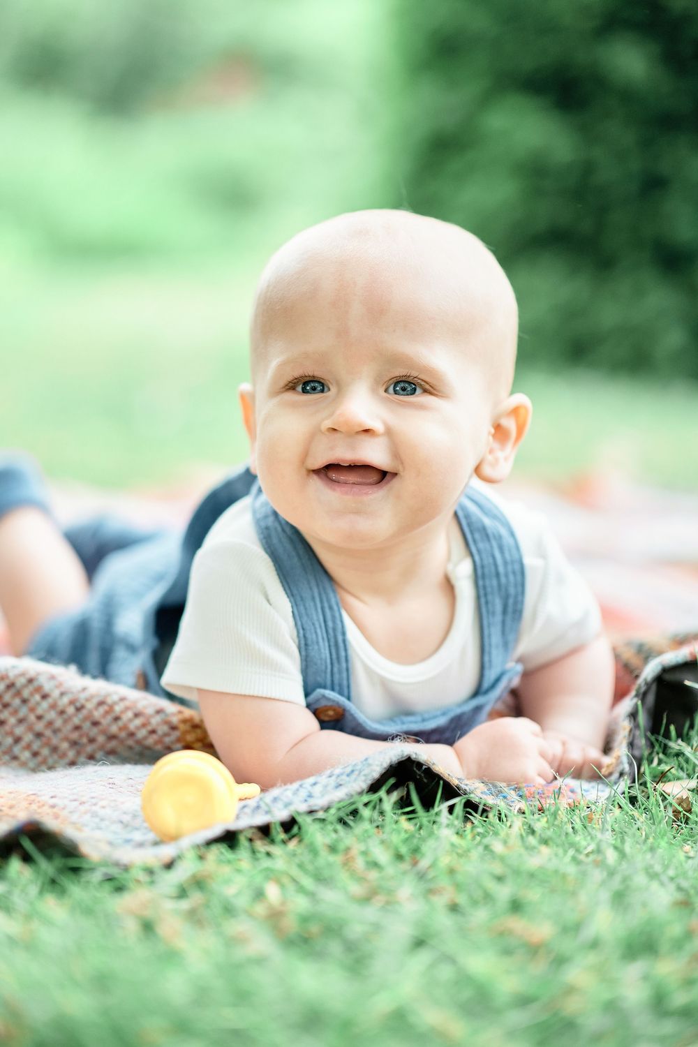 Happy baby lying on grass outside during sunny day with joyful expression.