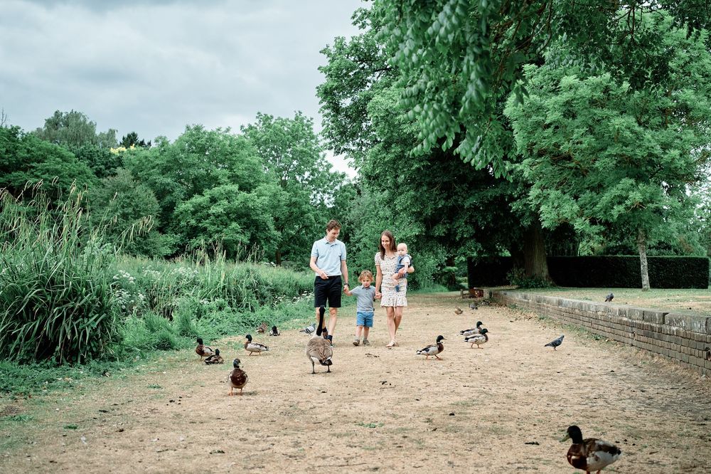 People walking with ducks on a dirt path surrounded by green trees and vegetation on a cloudy day.