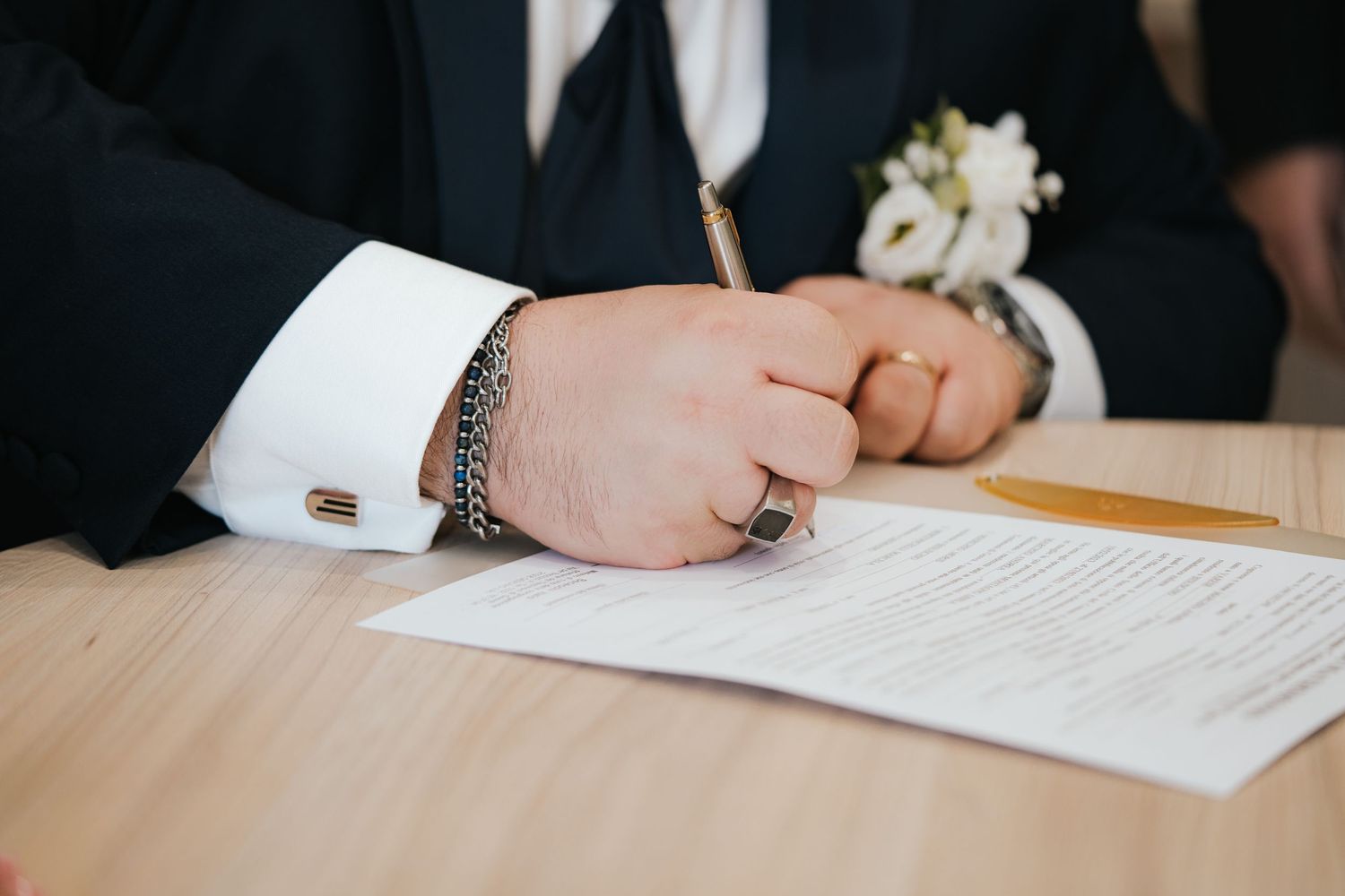 Close-up shot of hands signing wedding documents on a wooden surface.