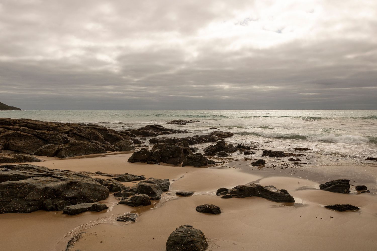 Moody seascape with rocky shoreline under cloudy skies at sunset.