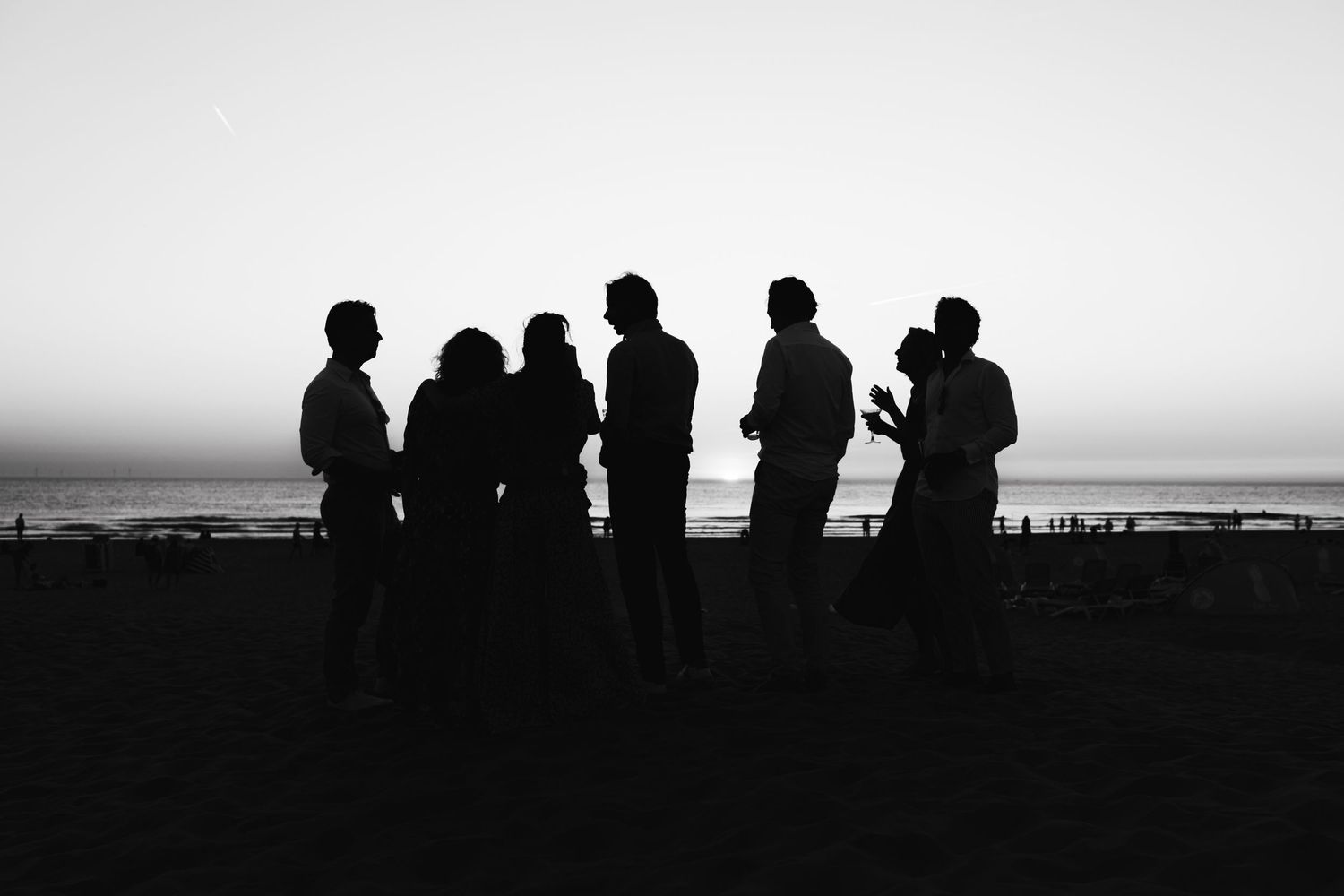 Silhouettes of six people standing together against a sunset sky at the beach.