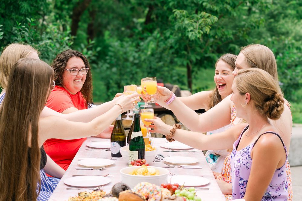 Group of friends chatting, toasting, and smiling at a garden party featuring blush gingham accents