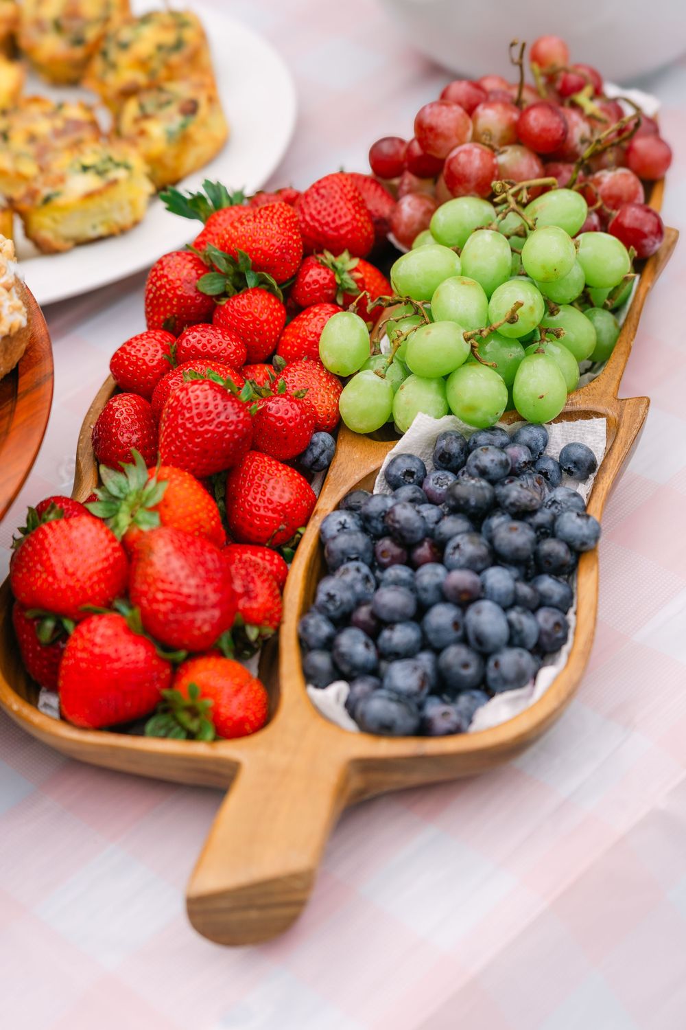 Close-up of a brunch table with fresh fruit and assorted doughnuts, styled with soft linens and garden greenery in the background