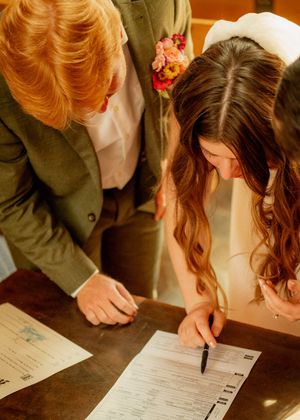 Newlyweds signing marriage documents together during their wedding ceremony.