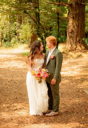 A romantic wedding portrait of a couple standing on a sunlit forest path.