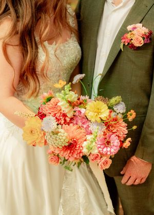 Close-up of a vibrant bridal bouquet with colorful dahlias and roses against wedding attire.