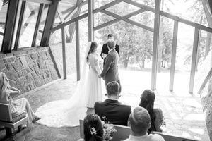 A wedding ceremony in progress inside a geometric glass chapel with guests seated.