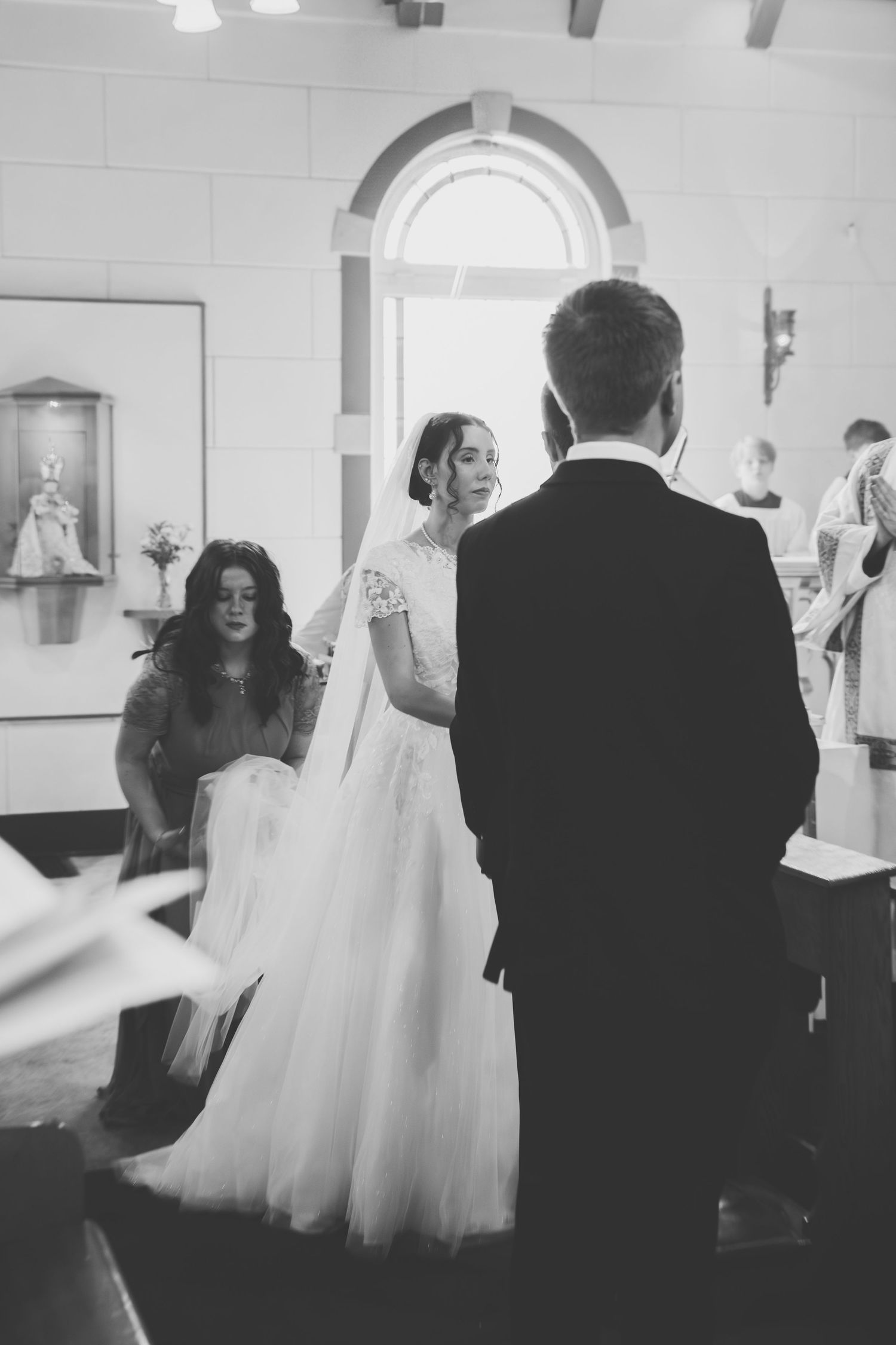 Black and white photo of wedding preparation scene with bridesmaids helping a bride in a flowing tulle gown.