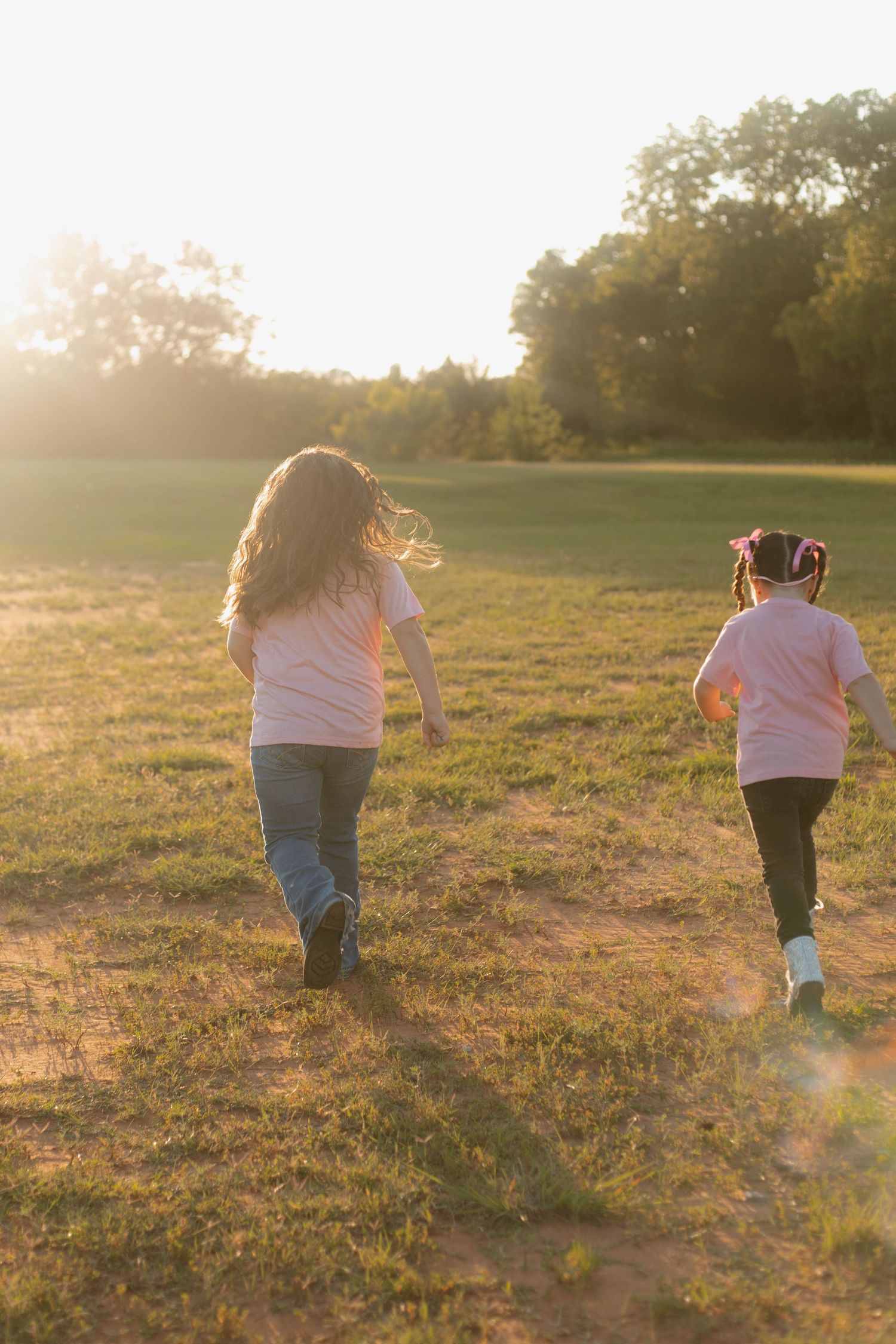 A family holds hands and dances together in a grassy field during golden hour sunset.