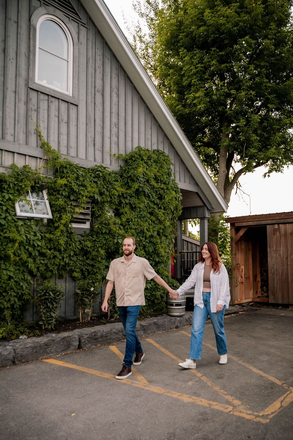 Couple strolling hand in hand by a rustic barn with ivy-covered walls and wooden architecture.