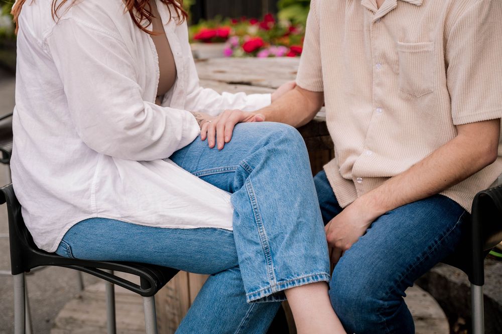 Two people wearing casual denim and white button-down shirts sit together in a close intimate moment.