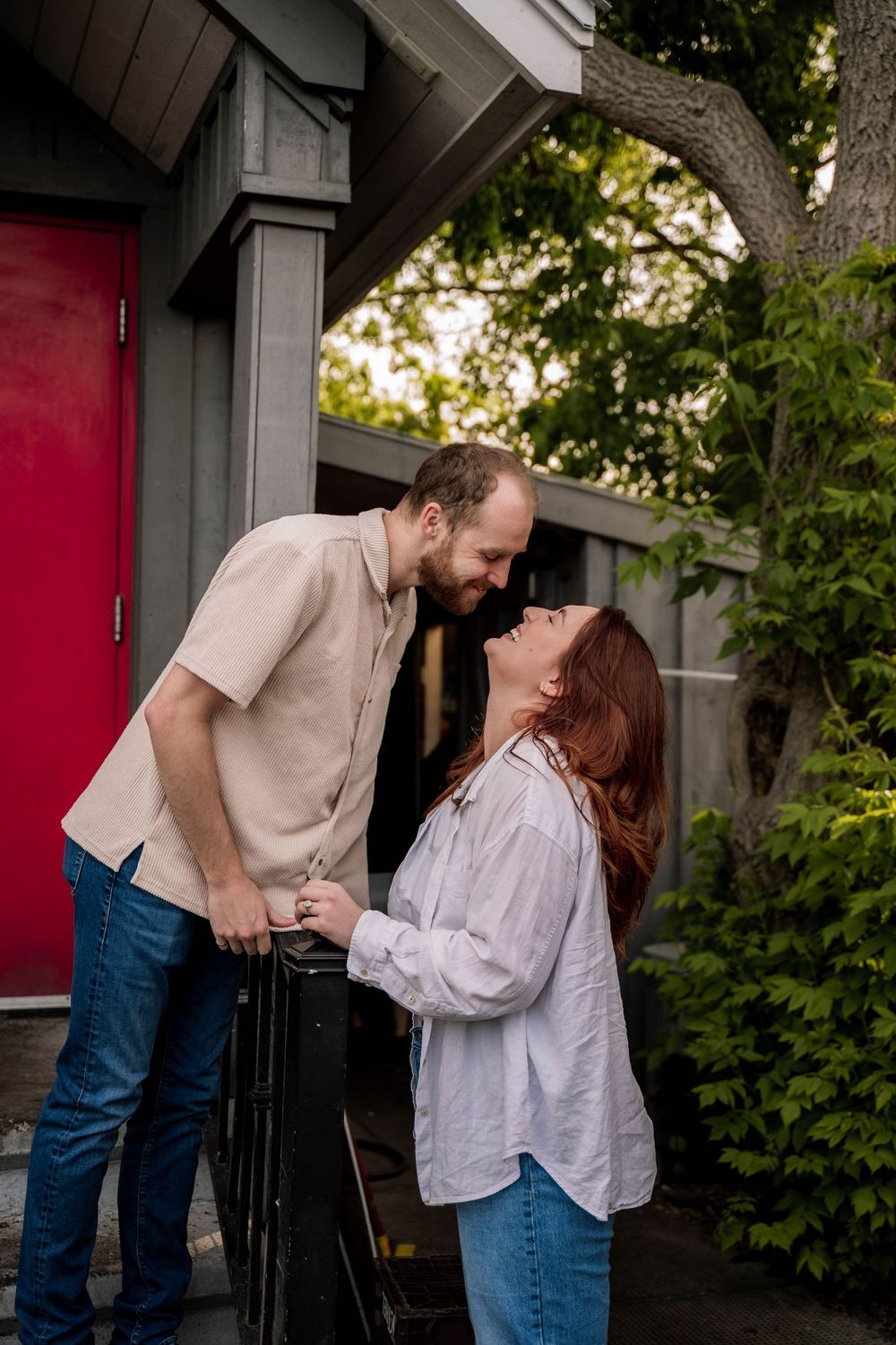 A romantic couple standing together near a doorway with a red door in a natural outdoor setting.