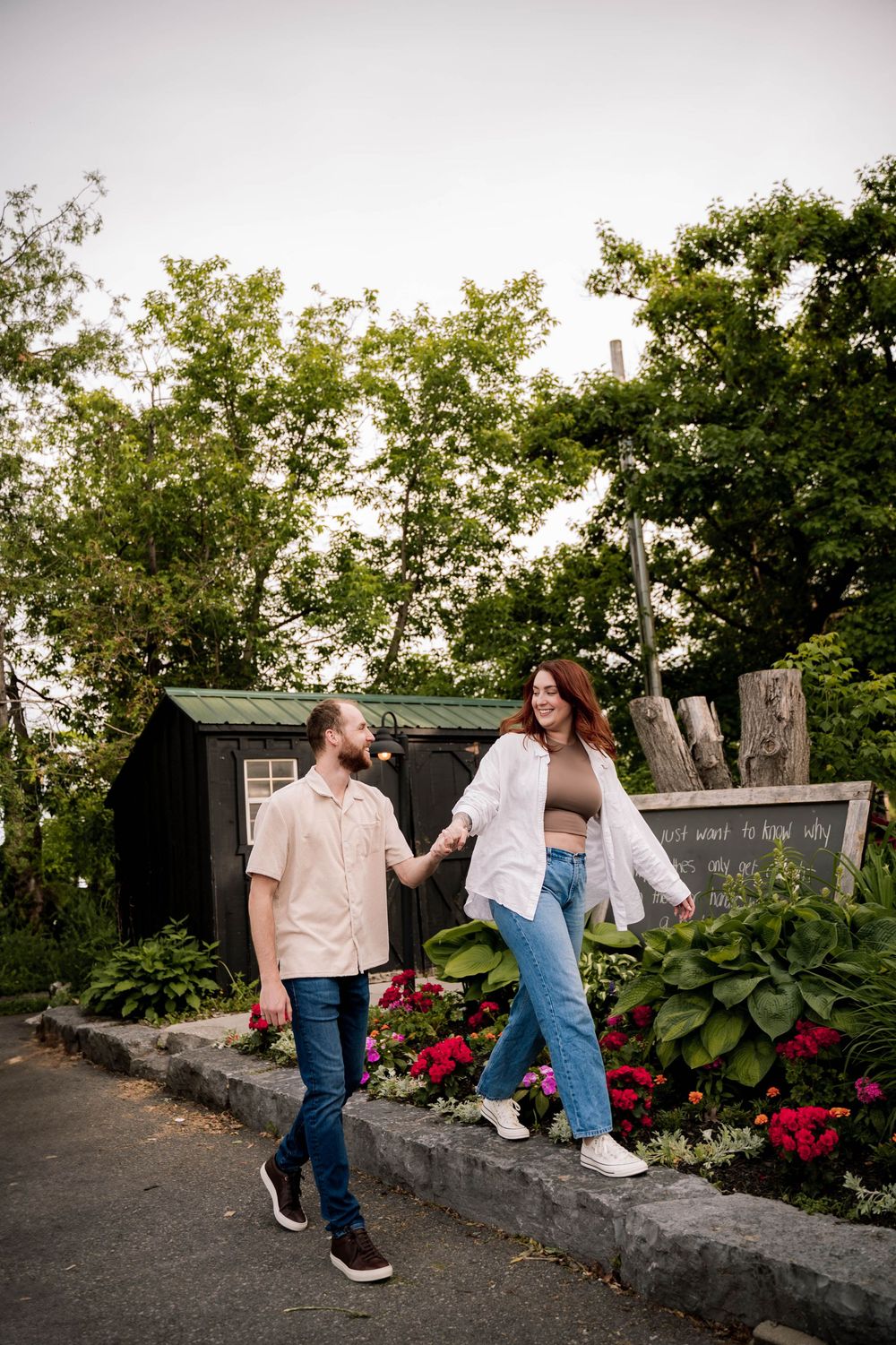 A couple walks hand in hand along a garden path with blooming flowers and greenery on a summer day.