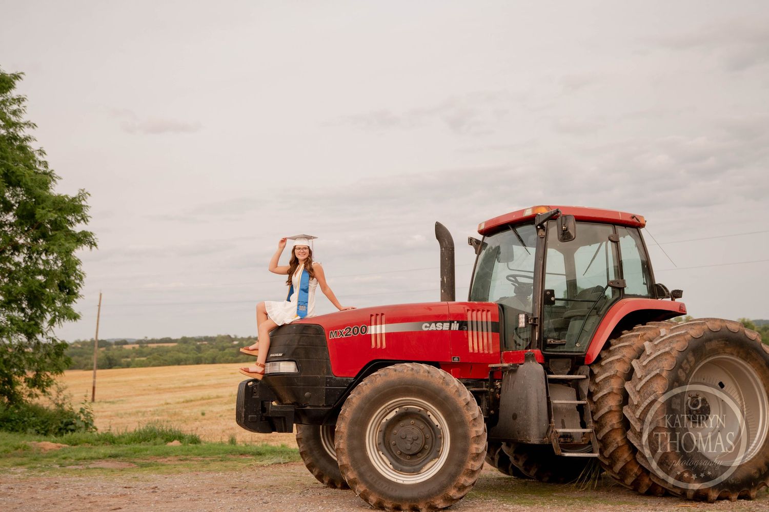 Red agricultural tractors line up on the edge of a farm field against cloudy sky and rural landscape.