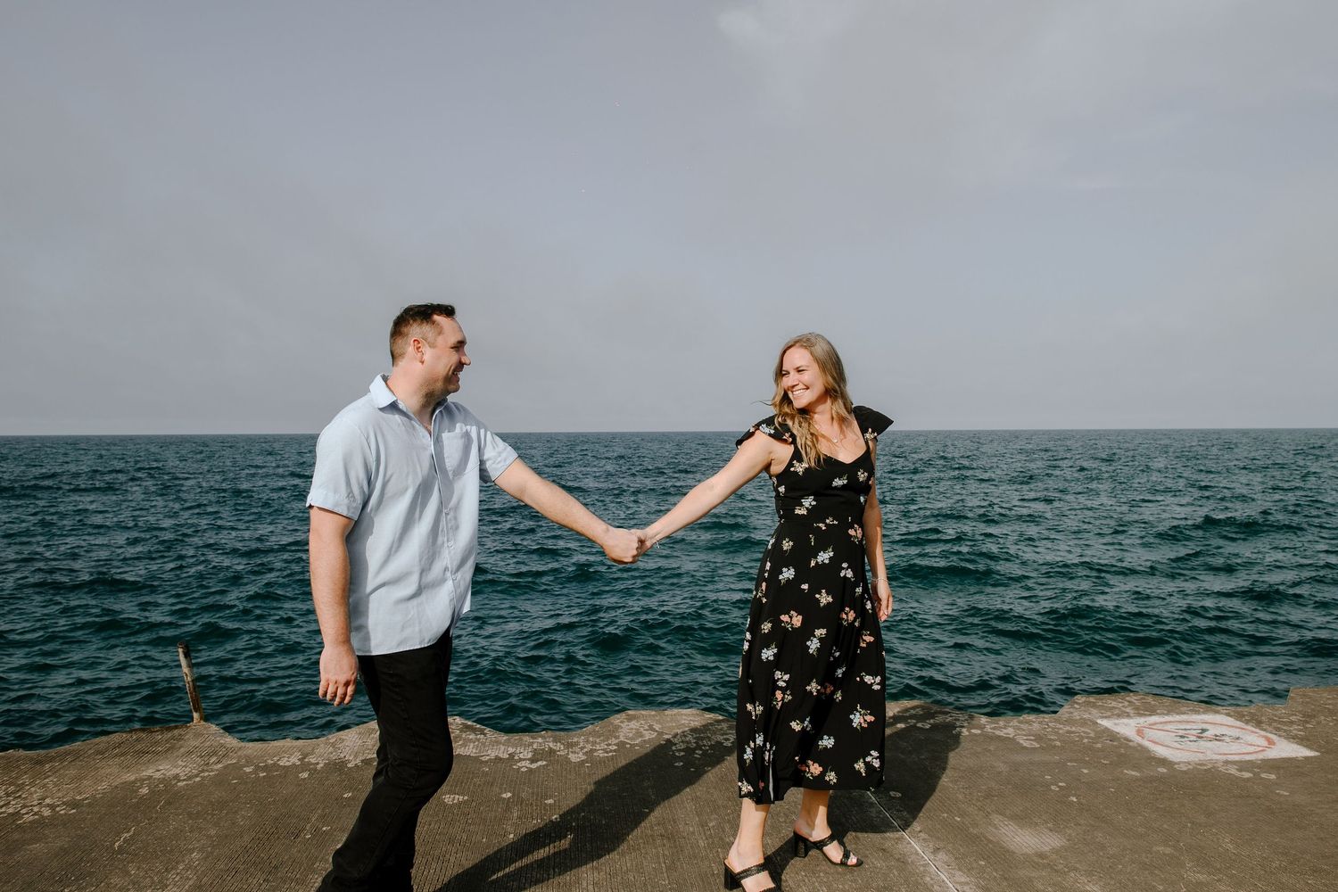 Couple holding hands and walking along rocky ocean shoreline on overcast day.