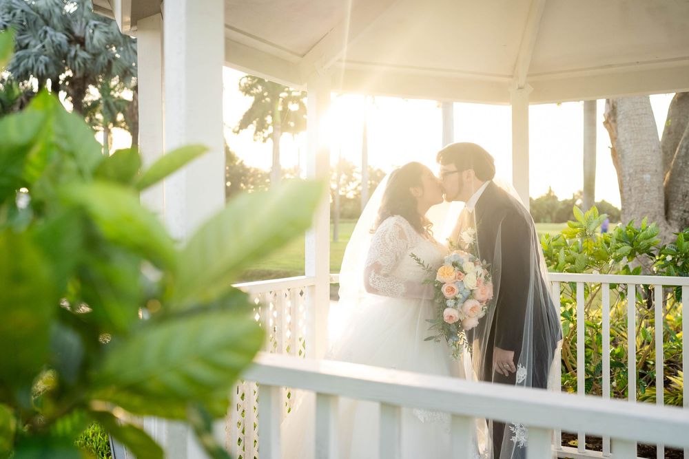 Wedding couple embraces under white gazebo draped with decorative bunting flags during outdoor ceremony.
