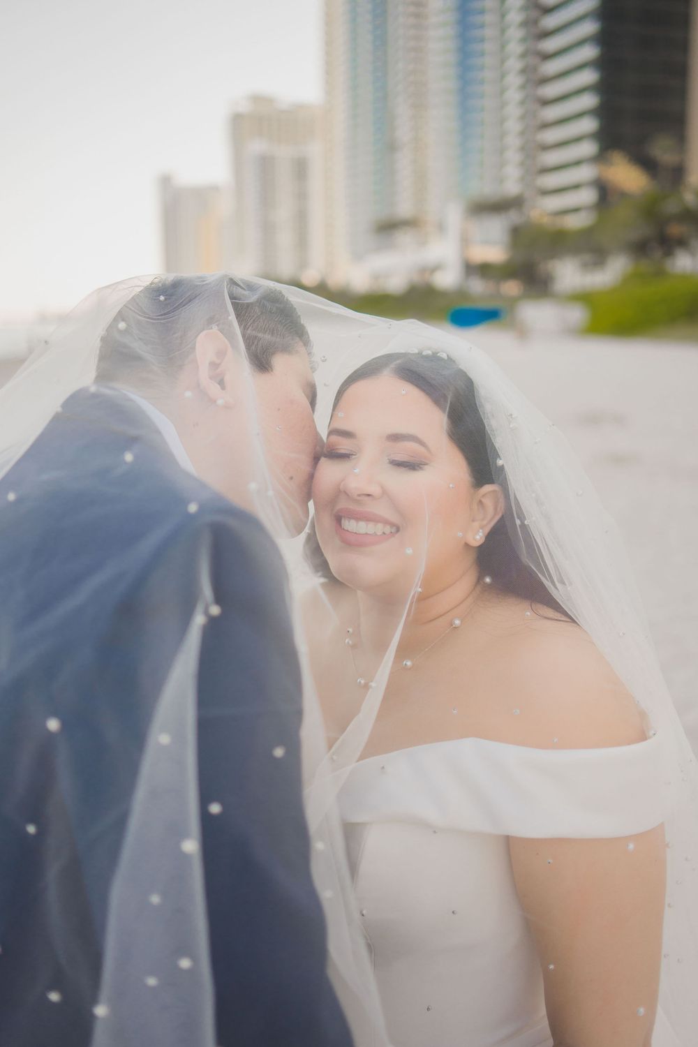 A romantic wedding moment captured with a veil flowing in the breeze along a coastal city skyline.