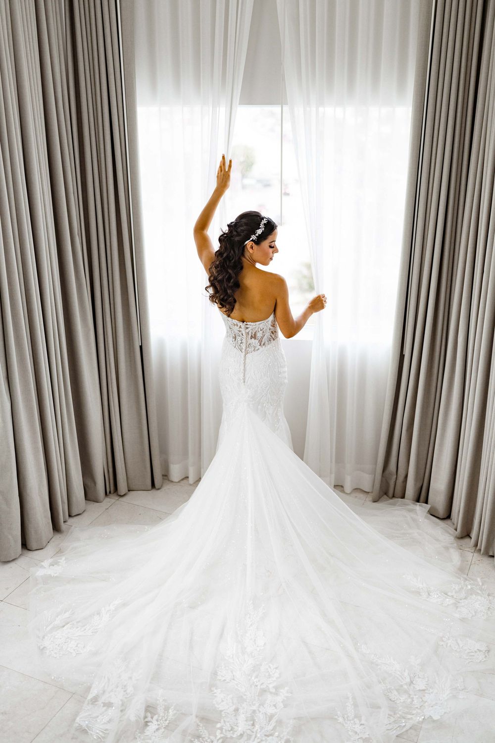Elegant mermaid wedding dress with lace details and long train photographed against light grey curtains.